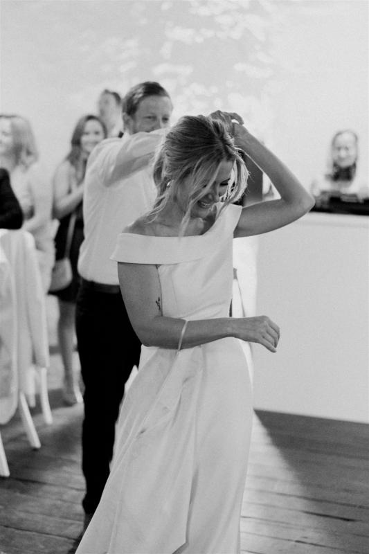 KWH real bride Shelley and Jack dance at their indoor reception. She wears the simple Lauren wedding dress with off the shoulder sleeve.