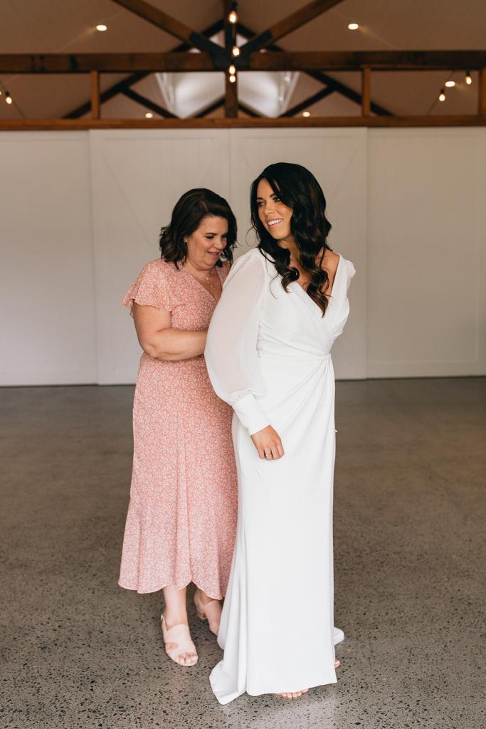 KWH real bride Rebekah has her bridesmaid do up the zipper back on her crepe Nikki gown, a simple fit and flare wedding dress.