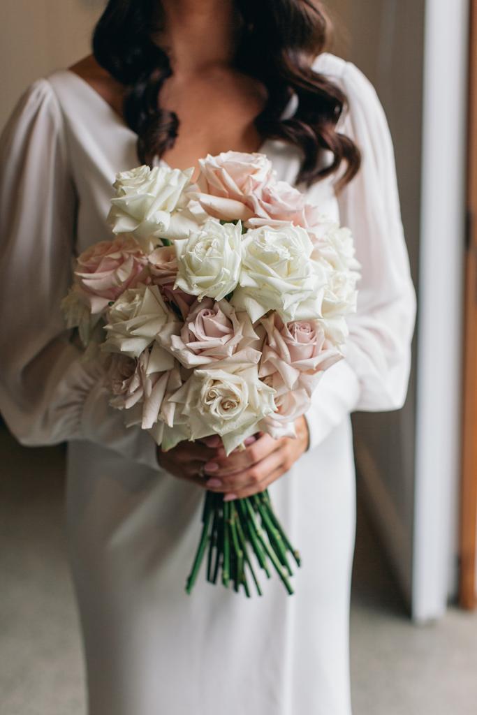KWH real bride Rebekah wears the chic Nikki wedding dress with long sleeves while holding her pale pink and white rose bouquet by Wren Floralista.