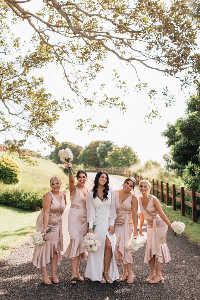 KWH real bride Rebekah and her bridesmaids cheer and celebrate. She wears the timeless Nikki wedding dress with sheer long sleeves.