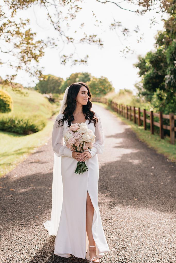 KWH real bride Rebekah stands in the road in her sleek Nikki wedding dress with long sleeves and long veil.