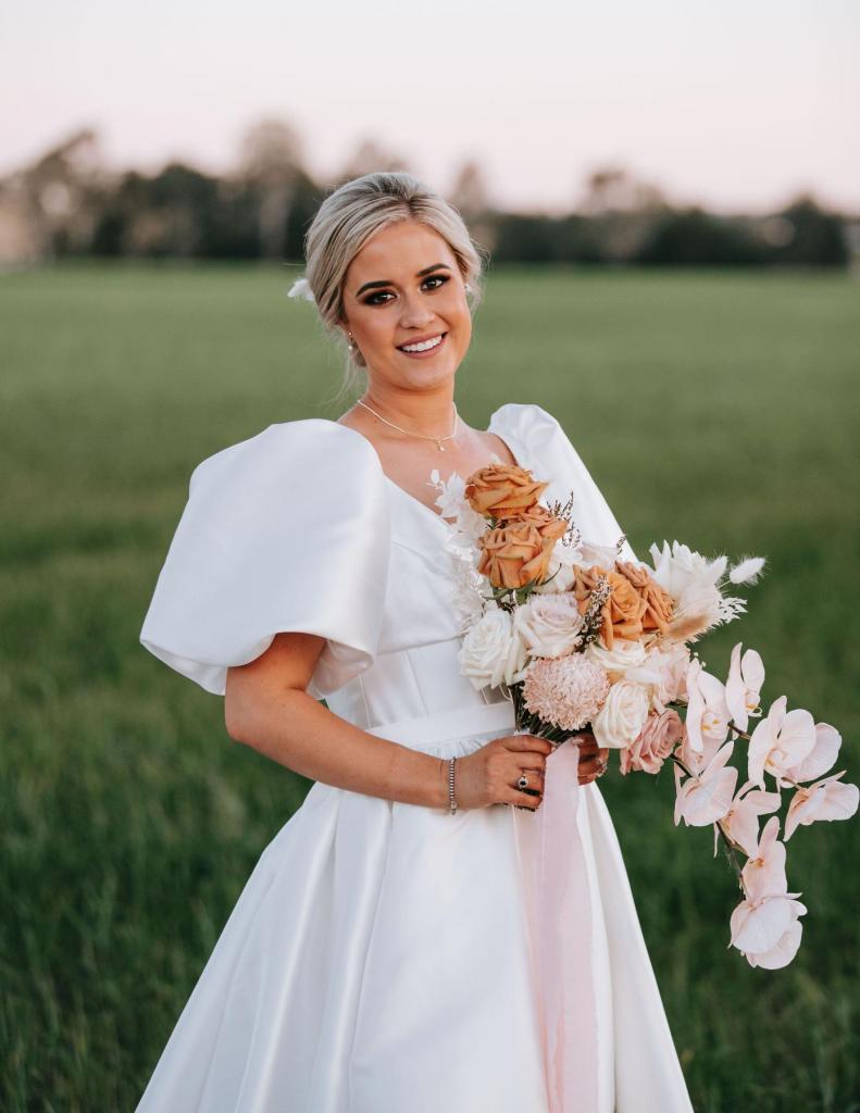 KWH real bride Izzy wearing the modern and bold Taryn Camille wedding dress; a aline silhouette wedding dress with fitted bodice. She holds a bouquet of orange and pink florals.