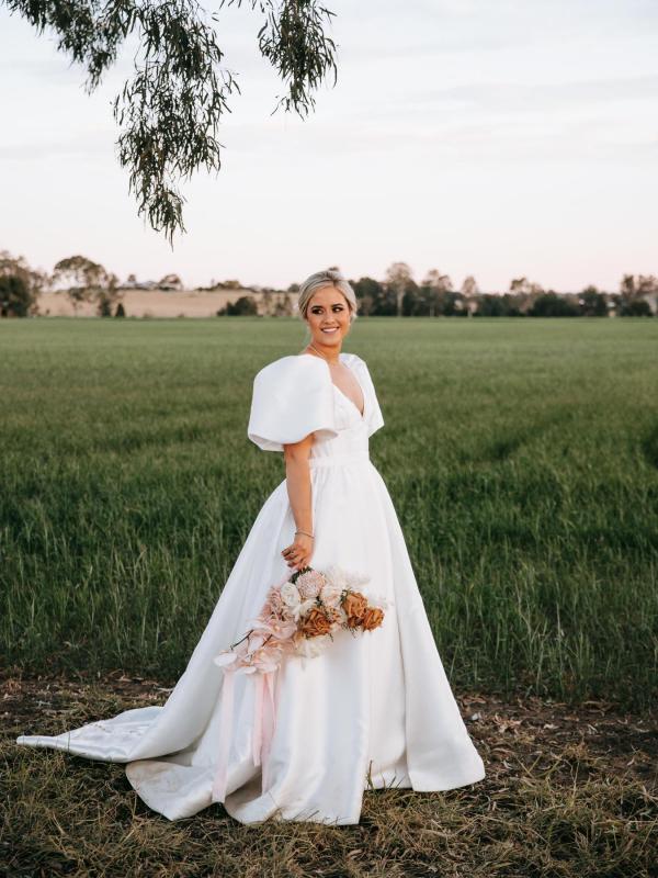 KWH real bride Izzy standing on the lawn in her stunning Taryn Camille wedding dress with over-sized sleeves.