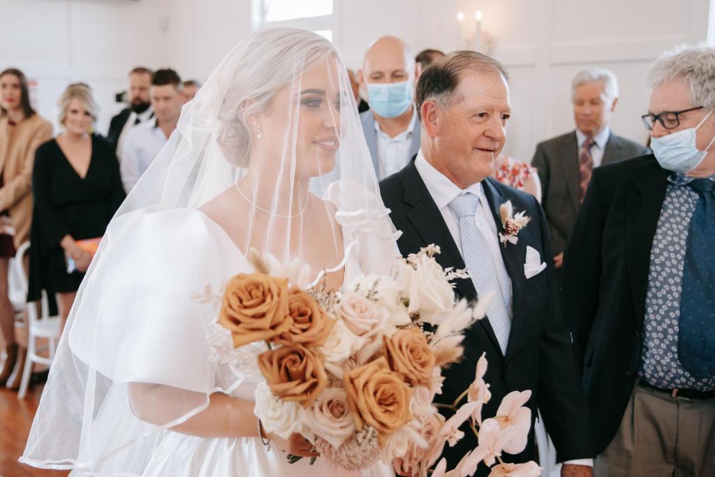 KWH real bride Izzy walking down the aisle with her dad with a veil over her face. She wears the classic Taryn Camille wedding dress with pockets.