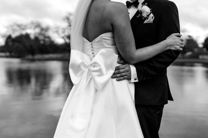 B&W image of KWH real bride Annabelle and Will staanding together showing off the oversized satin bow on the back of her Jacqueline Melanie gown, a modern a-line wedding dress.