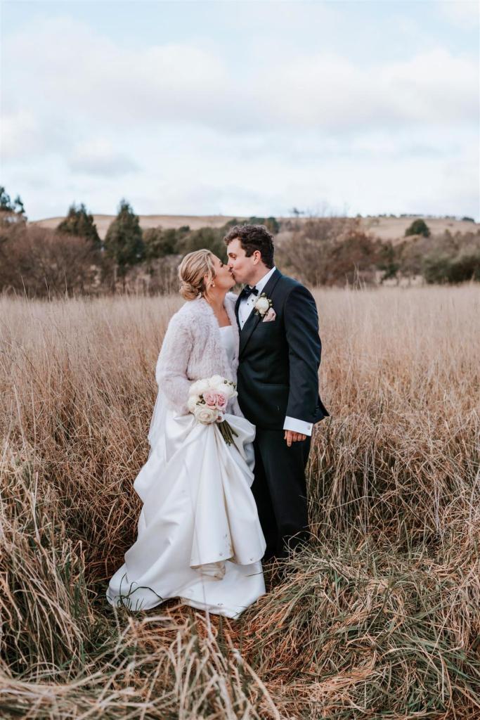KWH Real bride Annabelle and Will kiss in the dry field as she wears her classic Jacqueline Melanie gown, a strapless a-line wedding dress with fur cape.