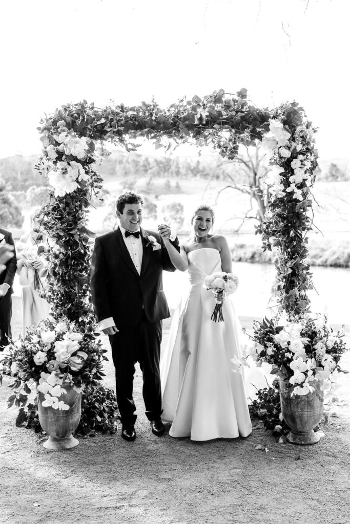 B&W image of KWH real bride Annabelle cheering with Will at the alter. She wears the modern Jacqueline Melanie gown, a strapless ballgown wedding dress.