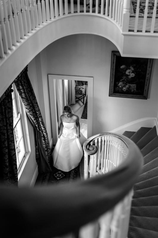 B&W image of KWH real bride Annabelle walking down a spiral staircase in her Jacqueline Melanie gown, a contemporary princess wedding dress with a-line skirt.