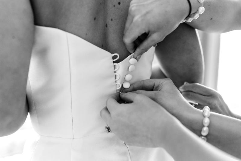 B&W image of KWH real bride Annabelle having her satin buttons done up on her Jacqueline Melanie gown, a modern bridal ballgown with a-line skirt.