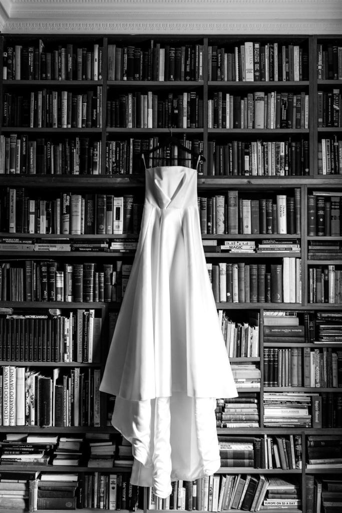 B&W image of KWH real bride Annabelle's Jacqueline Melanie gown hanging up on a bookcase. Jacqueline Melanie is a modern bridal ballgown with straightcut bodice