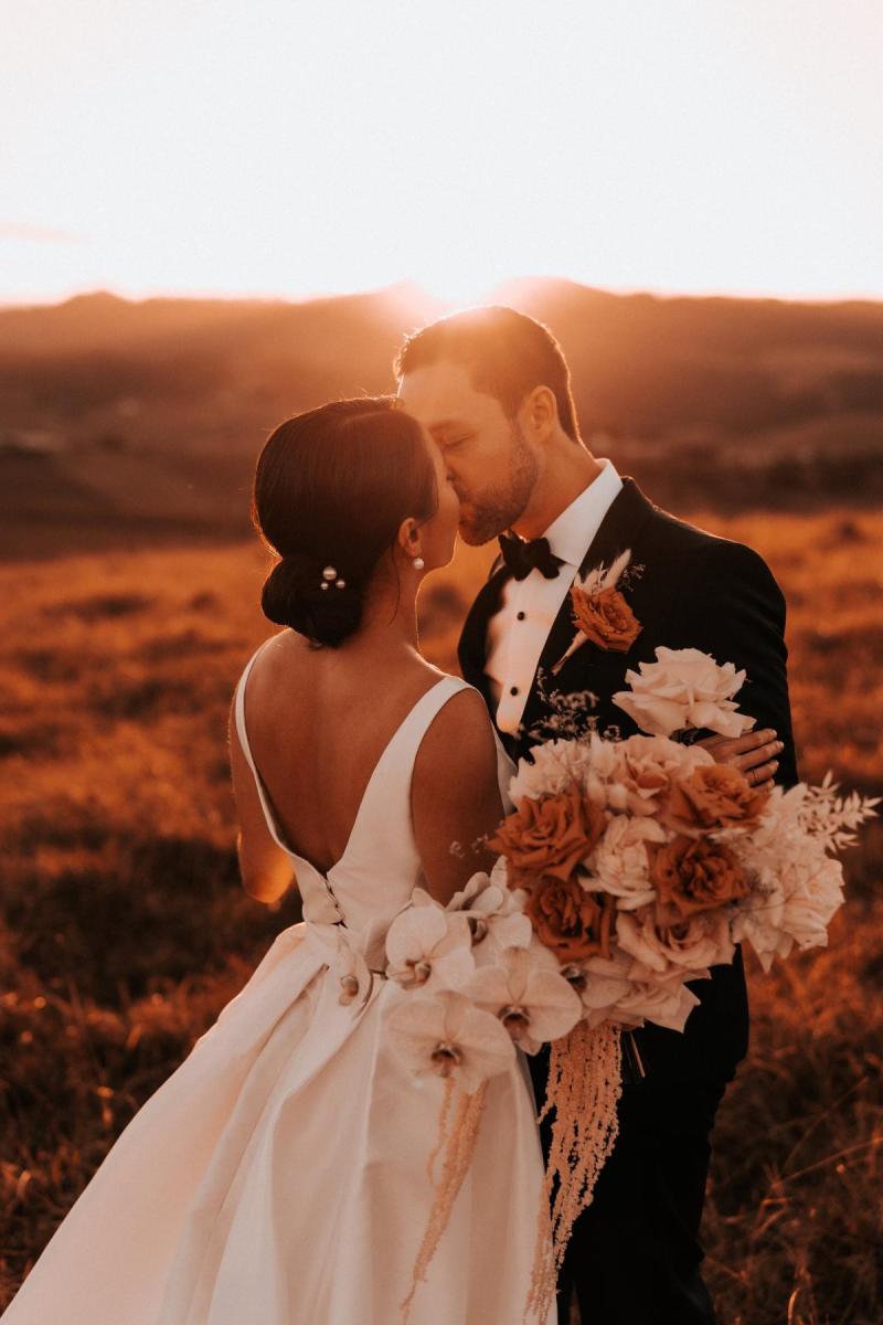 KWH real bride Rebecca and Matthew kiss under the sunset as she wears her Leonie Melanie gown, a modern princess wedding dress with V-neck.