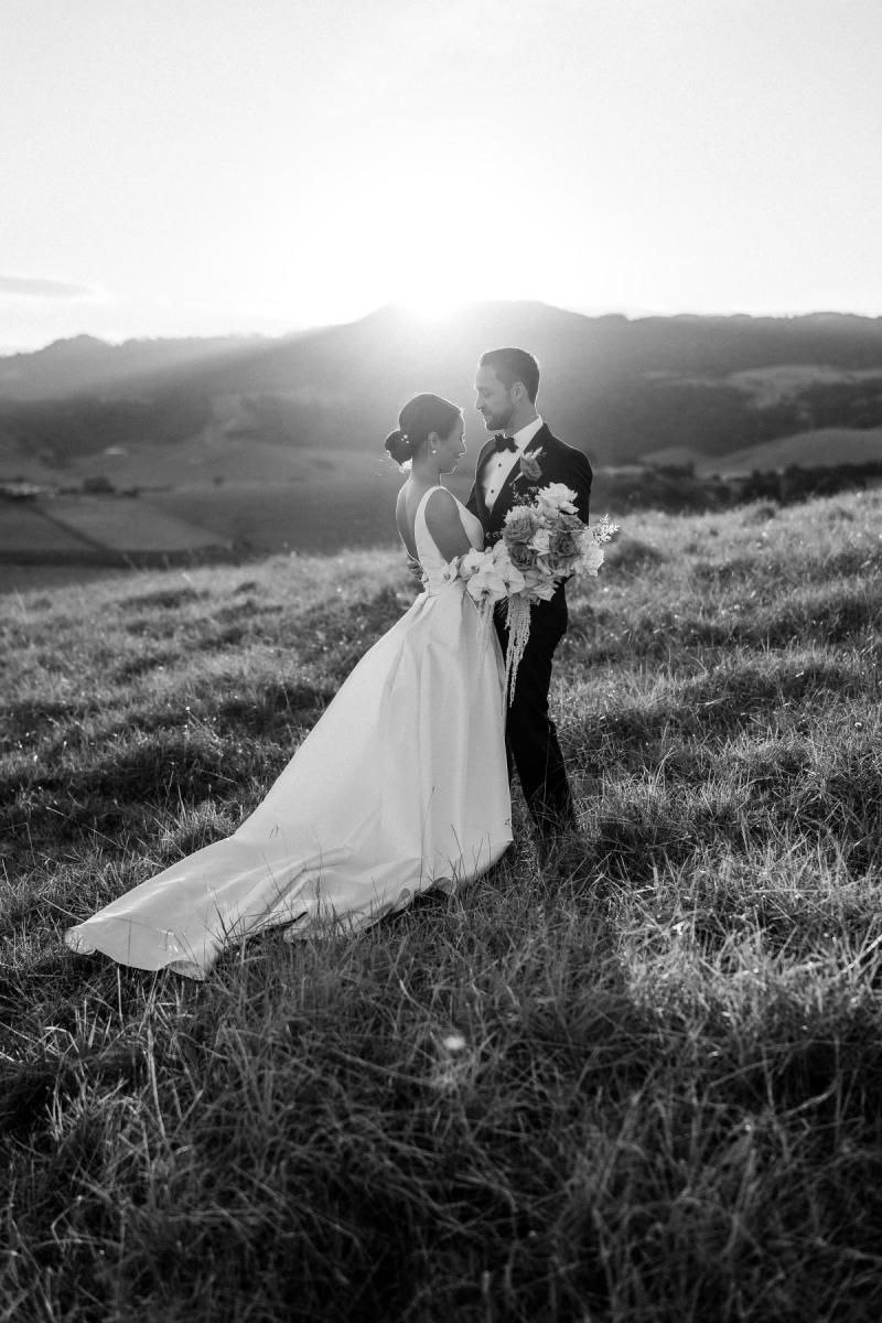 B&W image of KWH real bride Rebecca and Mattew standing on the hillside. She wears the classic Leonie Melanie gown, a V-neck open back a-line wedding dress.