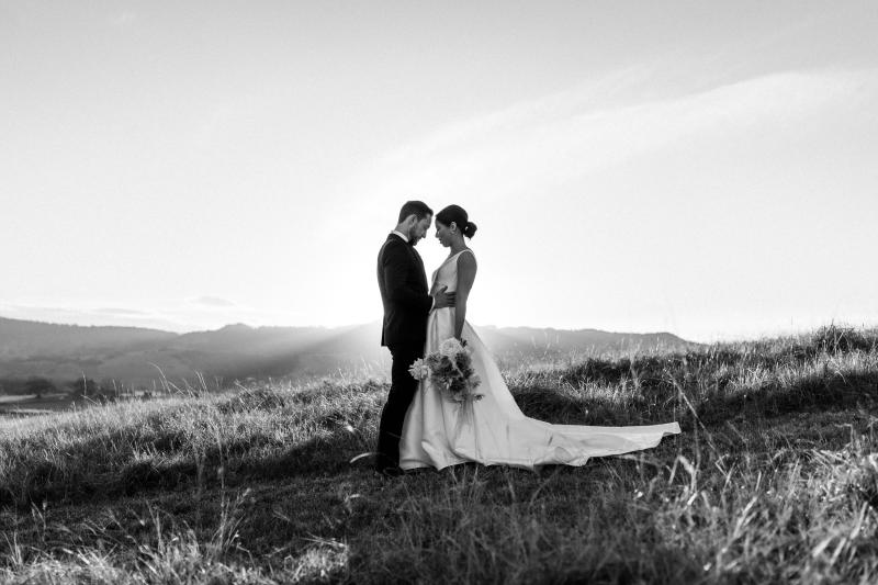 B&W image of KWH real bride Rebecca and Matthew on the hilltop as she stands in her timeless Leonie Melanie gown, a V-neck modern a-line wedding dress.