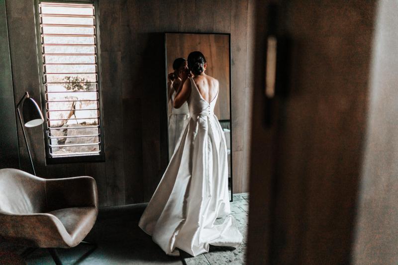 KWH real bride Rebecca secures her earrings as she dons the classic Leonie Melanie gown, a modern ballgown wedding dress with V-back