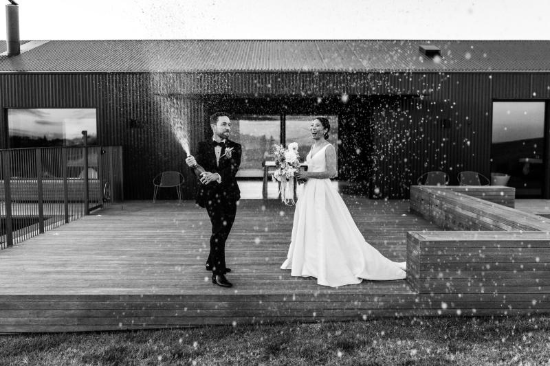 B&W image of KWH real bride Rebecca and Mattew standing on the hillside. She wears the classic Leonie Melanie gown, a V-neck open back a-line wedding dress.