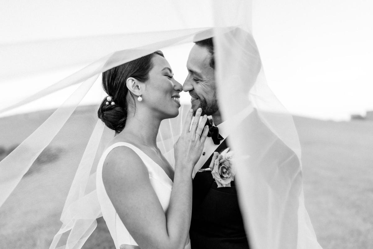 B&W image of KWH real bride Rebecca under the veil with her husband Matthew. She wears the Leonie Melanie gown, a classic ball gown wedding dress.