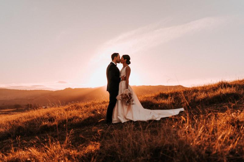 B&W image of KWH real bride Rebecca and Mattew standing on the hillside. She wears the classic Leonie Melanie gown, a V-neck open back a-line wedding dress.