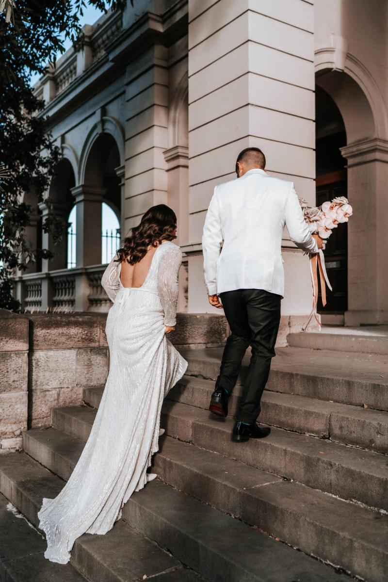 KWH real bride Katherine walks up the church stairs with Conor. She wears the gorgeous Margareta gown, a backless long sleeve beaded wedding dress.