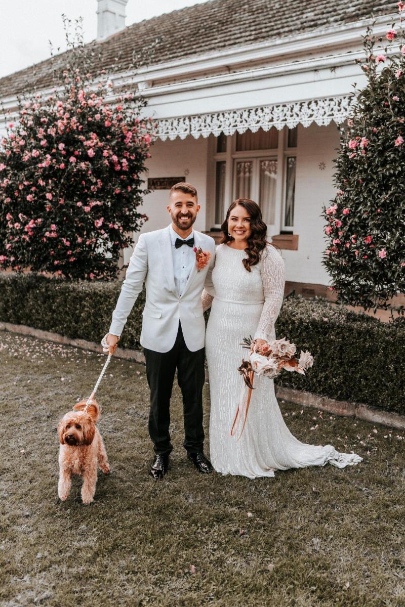 KWH real bride Katherine and Conor standing outside of Ravensthrope with their dog. She wears the Margareta gown, a high neck long sleeve wedding dress.