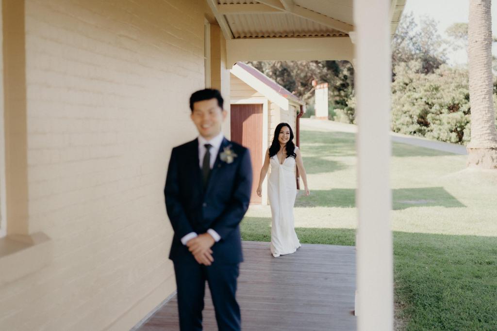 KWH real bride Vicki walking towards Tom for their first look. She wears the Arabella gown, plunging neckline simple sheath wedding dress.
