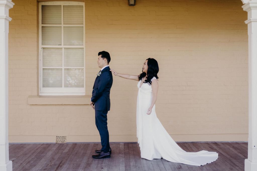 KWH Real bride Vicki taps Tom's shoulder during their first look. She wears the Arabella gown, plunging neckline simple sheath wedding dress..