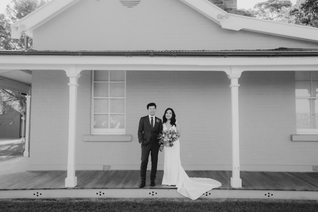 B&W image of KWH real bride Vicki and Tom standing on a porch together. She wears the Arabella gown, plunging neckline simple wedding dress.