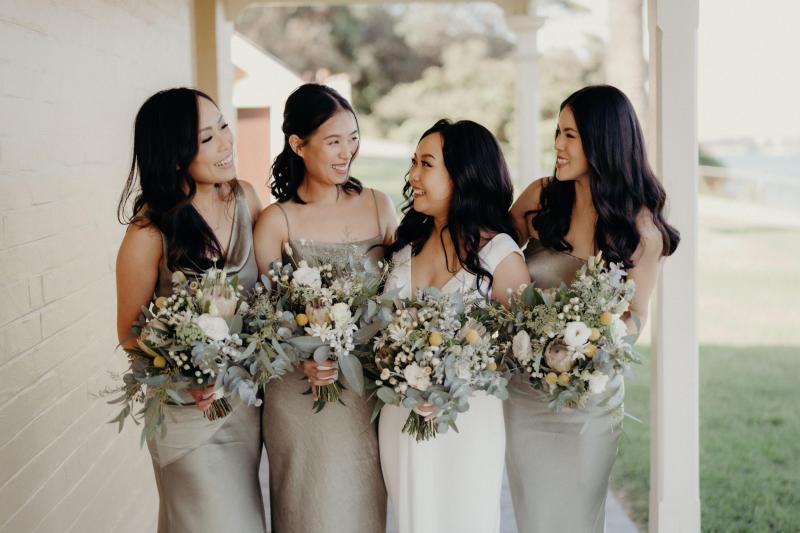 KWH real bride Vicki stands with her bridesmaids on the porch. They wears sage green bridesmaids dresses and she wears the Arabella gown, lunging neckline simple wedding dress.