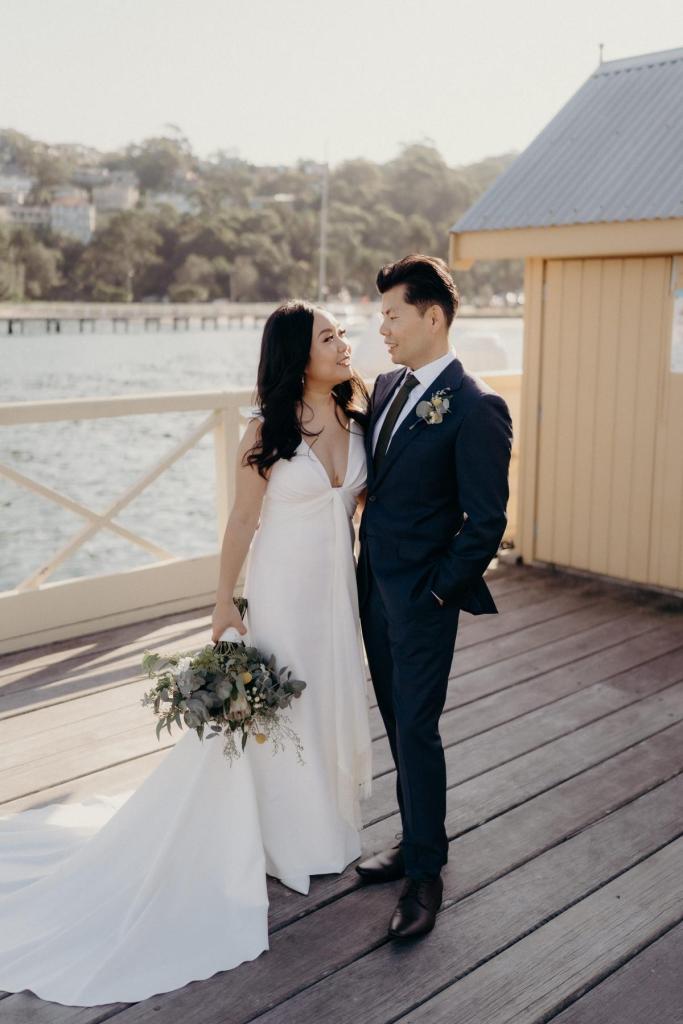 KWH real bride Vicki and tom hug on a dock. She wears the Arabella gown, lunging neckline simple wedding dress.