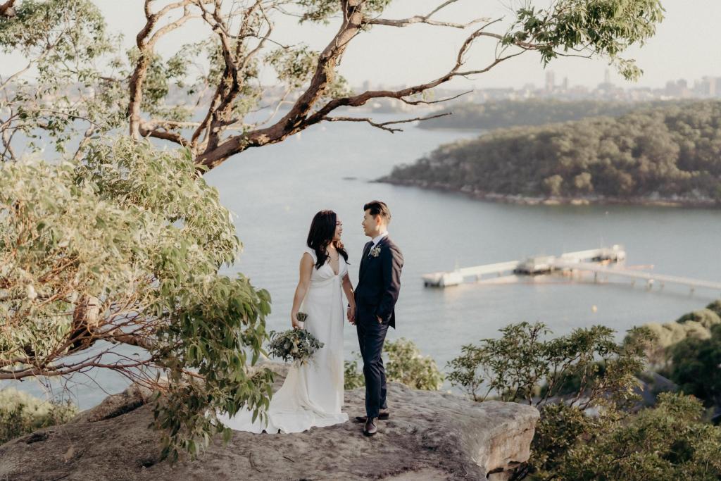 KWH real bride Vicki and Tom standing on a cliff edge. She wears the Arabella gown, lunging neckline simple wedding dress.