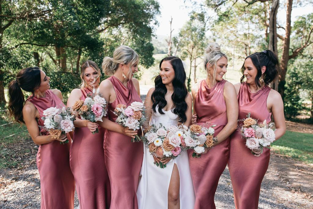 KWH real bride Hannah stands with her bridesmaids who wear pink silk slip dresses. She wears the Blake Camille gown, a modern strapless aline wedding dress.