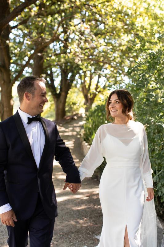 KWH Real bride Erin walks hand-in-hand with Stephen through the woods. She wears the modern Brie gown, simple wedding dress with high neck and long sleeves..