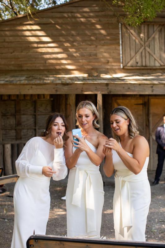 KWH real bride Erin applies lipstick with her bridesmaids. She wears the modern Brie gown, simple wedding dress with high neck and long sleeves.