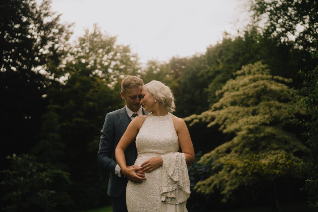 KWH real bride Laura and David embrace in their own secret garden. She wears the Cindy gown, a halter neck sequin wedding dress.