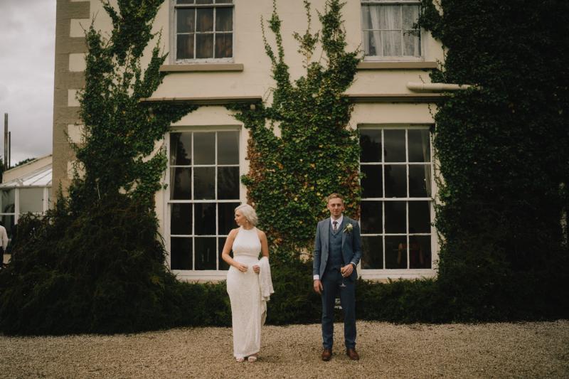 KWH real bride Laura and David stand in front of the Castel Grove Country house. She wears the Cindy gown, a halter neck sequin wedding dress.