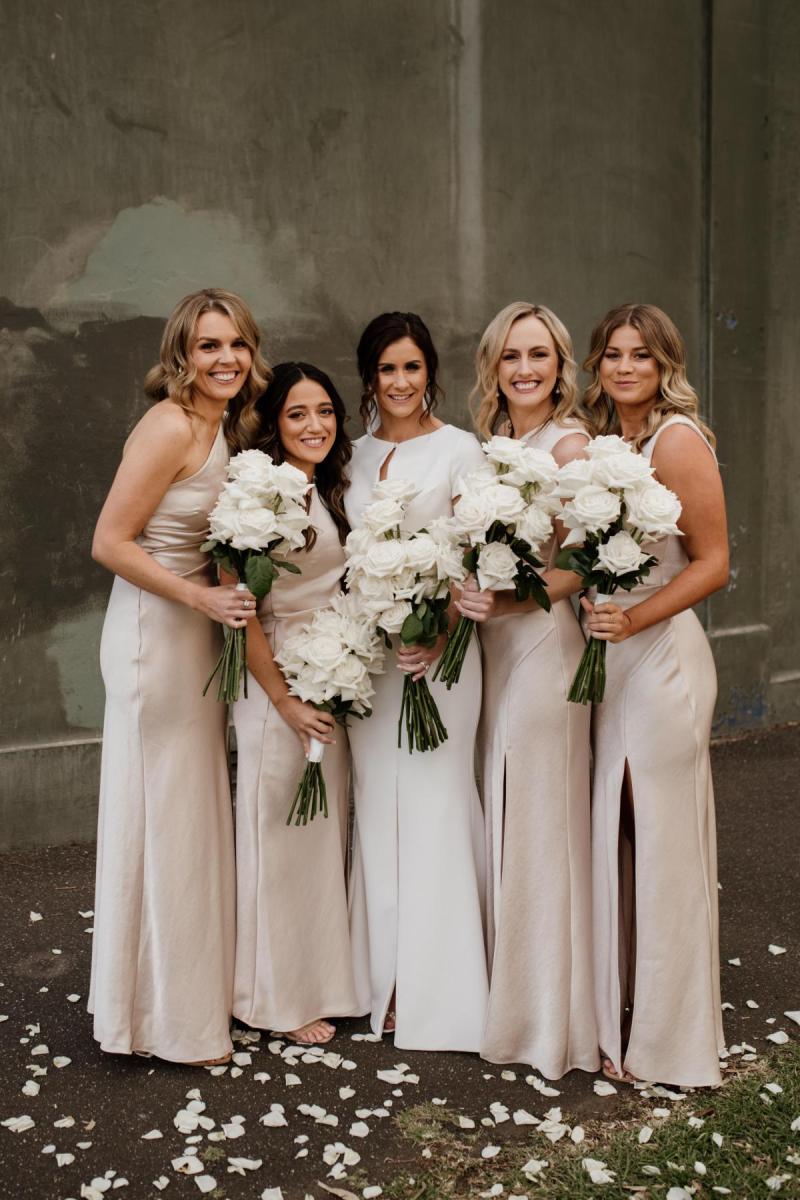 KWH real bride Jacqui stands with her bridesmaids who wear silk dresses. She wears the Clarissa gown, a high back fit and flare cap sleeve wedding dress.