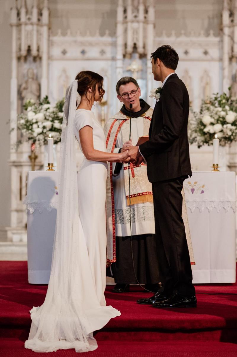 KWH real bride Jacqui stands at the altar with Chris as she wears the crepe Clarissa gown, a fit and flare cap sleeve modern wedding dress.