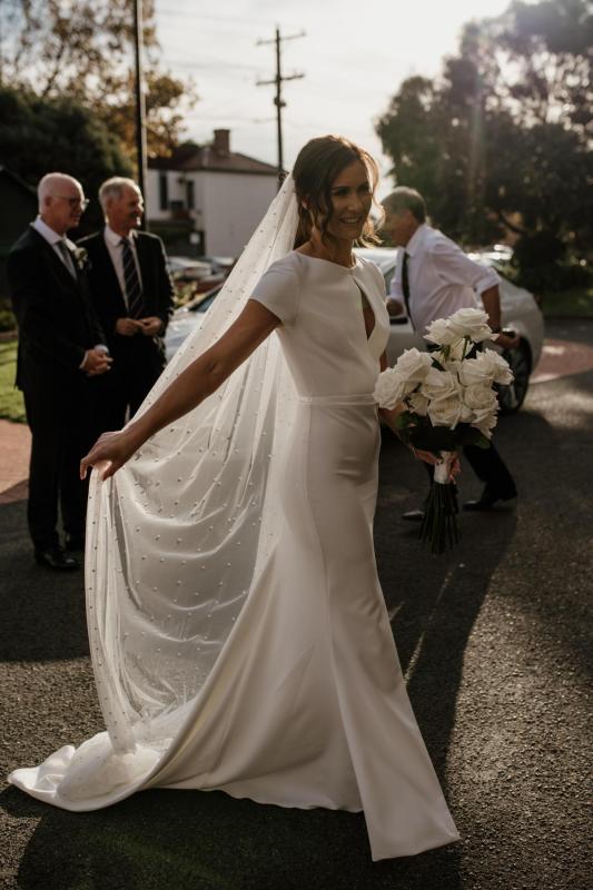 KWH real bride Jacqui walks with her Clarissa gown, a high neck modern fit and flare wedding dress with long pearl veil.