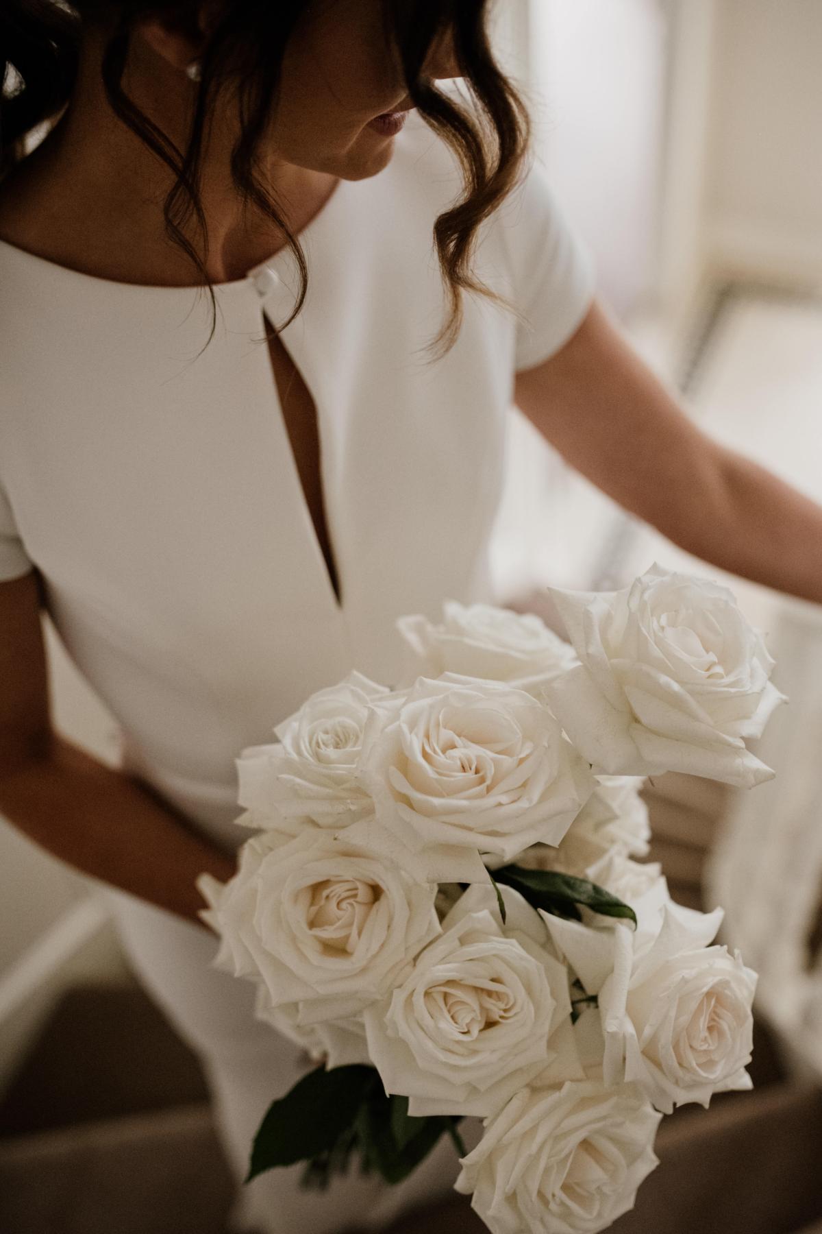 Image of KWH real bride Jacqui holding her white rose bouquet in her Clarissa gown, a modern fit and flare cap sleeve wedding dress.