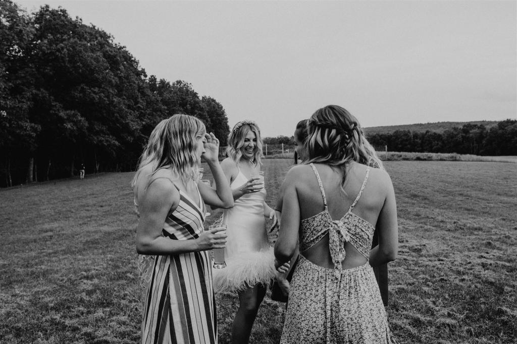 B&W photo of KWH real bride Kasey showing off her Sherry mini gown to her friends. Sherry mini is a simple short wedding dress with open back and feather detail.
