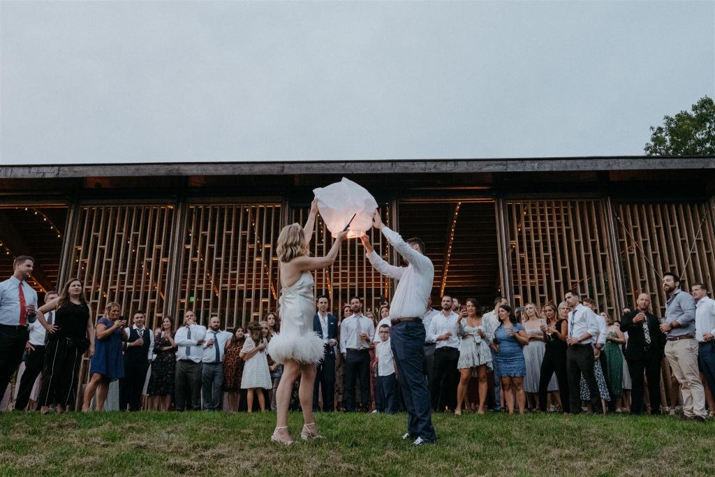 KWH real bride Kasey and Brian lighting a lantern to let go. She's wearing the Sherry mini gown, simple short wedding dress with open back and feather detail.