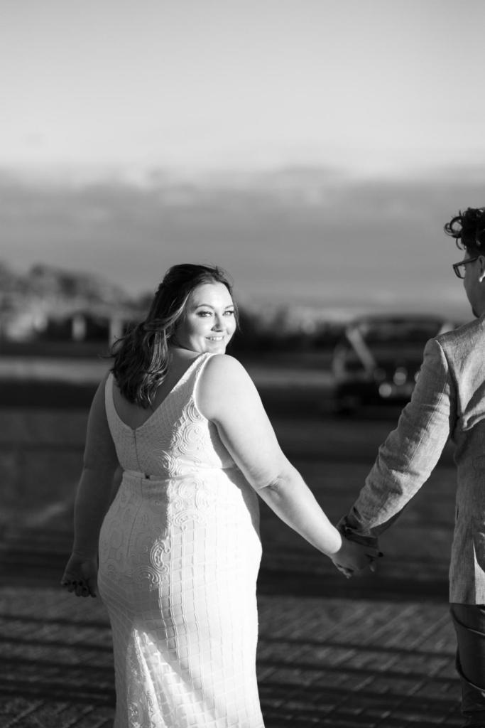 B&W image of KWH real bride Meg looking back at the camera in her Bobby gown, a fit and flare modern wedding dress.