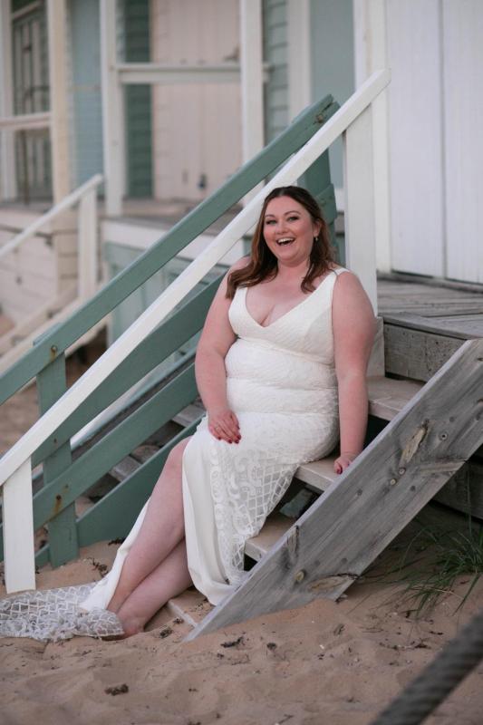 KWH real bride Meg smiling on the steps of the beach cabins. She wears the Bobby gown, a curve fit and flare wedding dress.