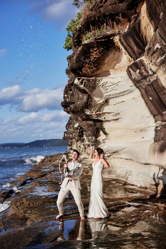 KWH real bride Emma and Will pop the champagne on the beachside as she wears the modern Rylie gown, an effortless lace fit and flare wedding dress.