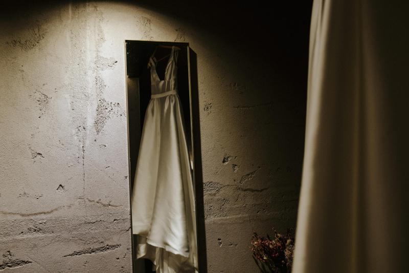 KWH real bride Tara's Taryn Camille gown hanging in front of a mirror. Taryn Camille is a modern a-line wedding dress with U-shaped neckline.