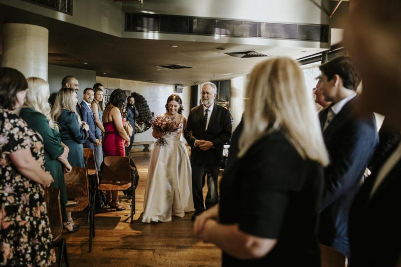 KWH real bride Tara walks down the aisle with her dad in her Taryn Camille gown; a classic aline wedding dress with bold neckline.