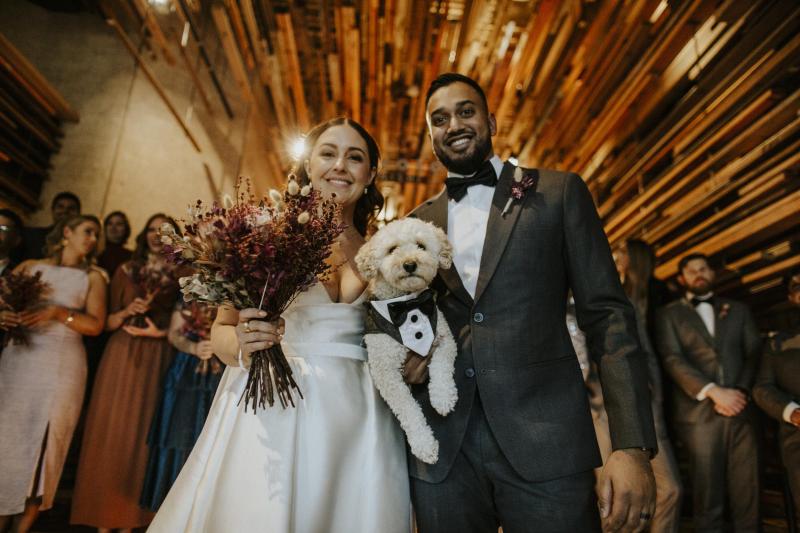 KWH real bride Tara and Chris pose with her dog in a tux. She wears the Taryn Camille gown, a grand aline wedding dress with high leg split.