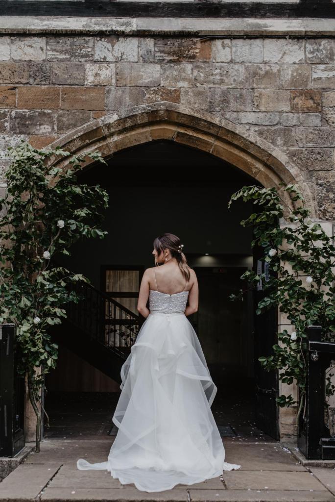 KWH real bride Monica stands in the castle arches in her Anya gown, a minimalist sequin wedding dress with Diamonds detachable train.