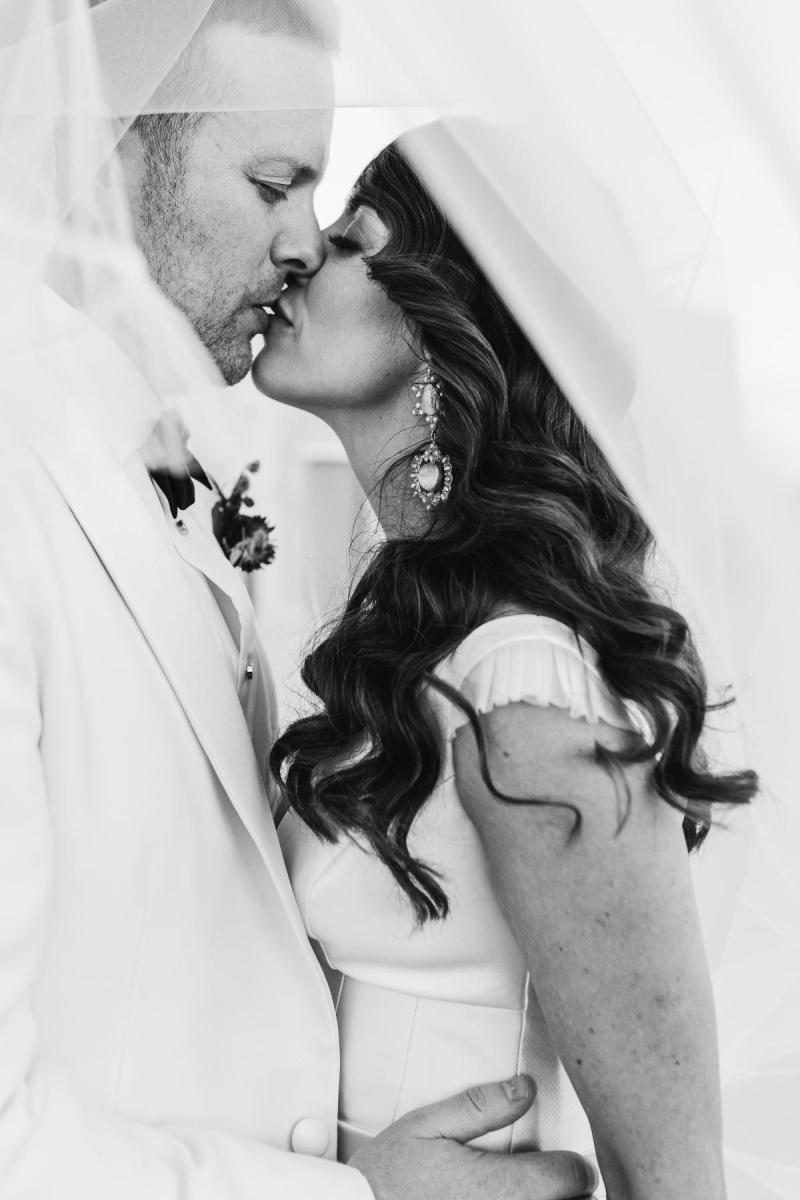 B&W image of KWH real bride Josey and Brad kissing. she wears the modern Taryn Camille gown, a timeless aline wedding dress with custom cap sleeves.