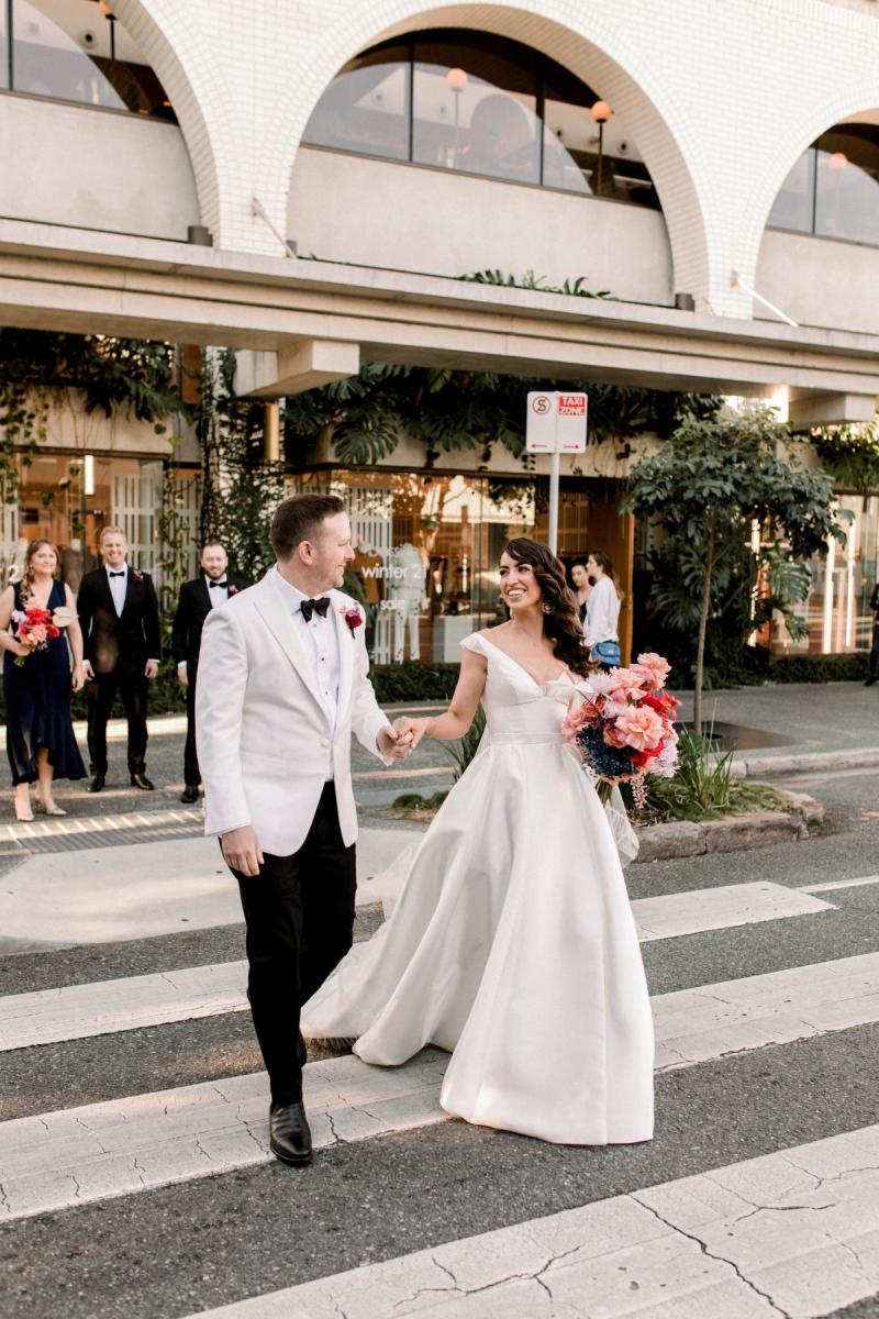 KWH real bride Josey and Brad walk across the street as she wears her flowy Taryn Camille gown, a modern aline wedding dress with U-shaped neckline.