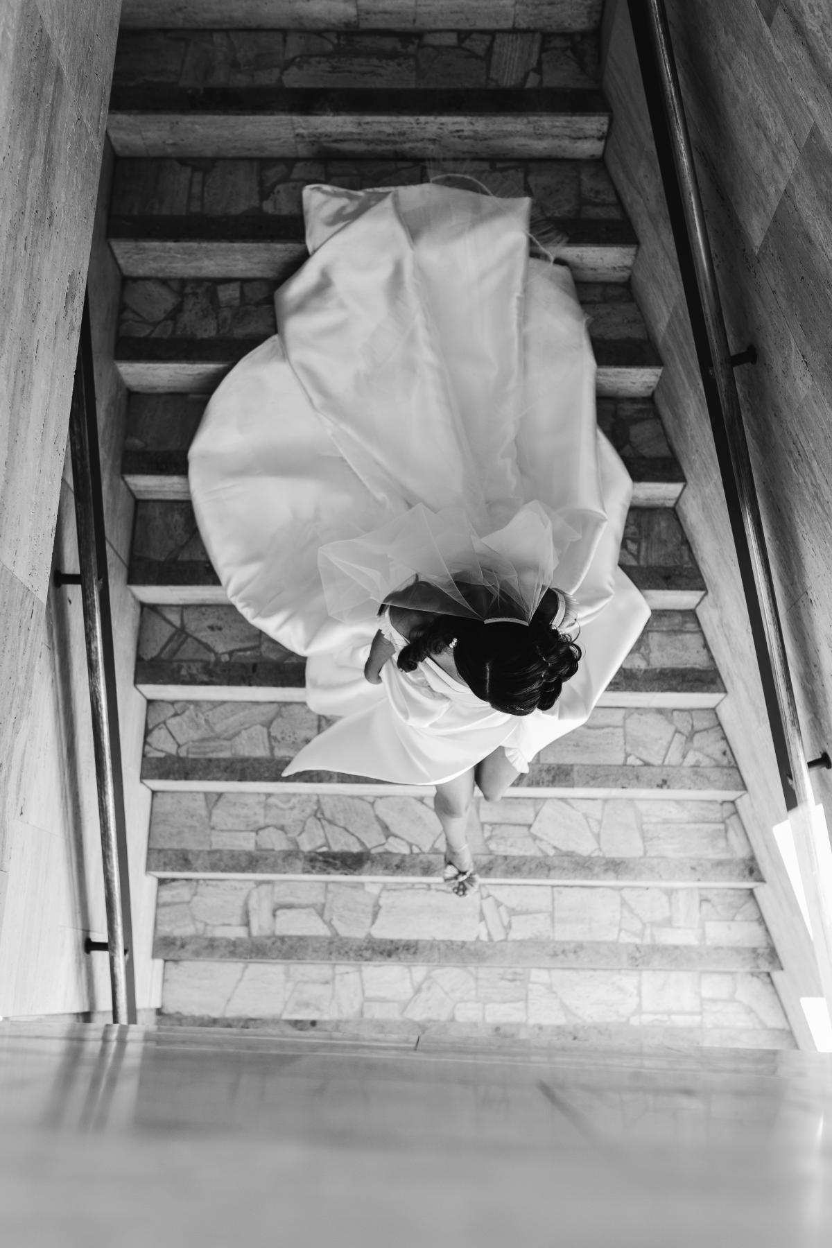 B&W image of KWH real bride Josey walking down the stairs in her glamorous Taryn Camille gown, a modern aline wedding dress with U-shaped neckline.